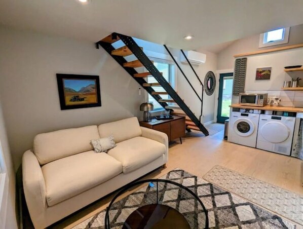 A living room with a sofa, a staircase, a washing machine, and a kitchen area.
