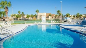 Une piscine d’un bleu éclatant, avec des chaises longues et, au fond, un court de tennis.
