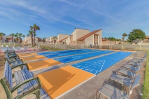 A shuffleboard court with seating and a building in the background. - Horizon South (Panama City Beach)
