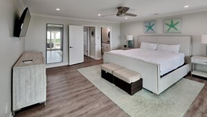 Ein Schlafzimmer mit einem großen Bett, einem Deckenventilator, einem an der Wand montierten Fernseher und einer Tür zu einem weiteren Zimmer.