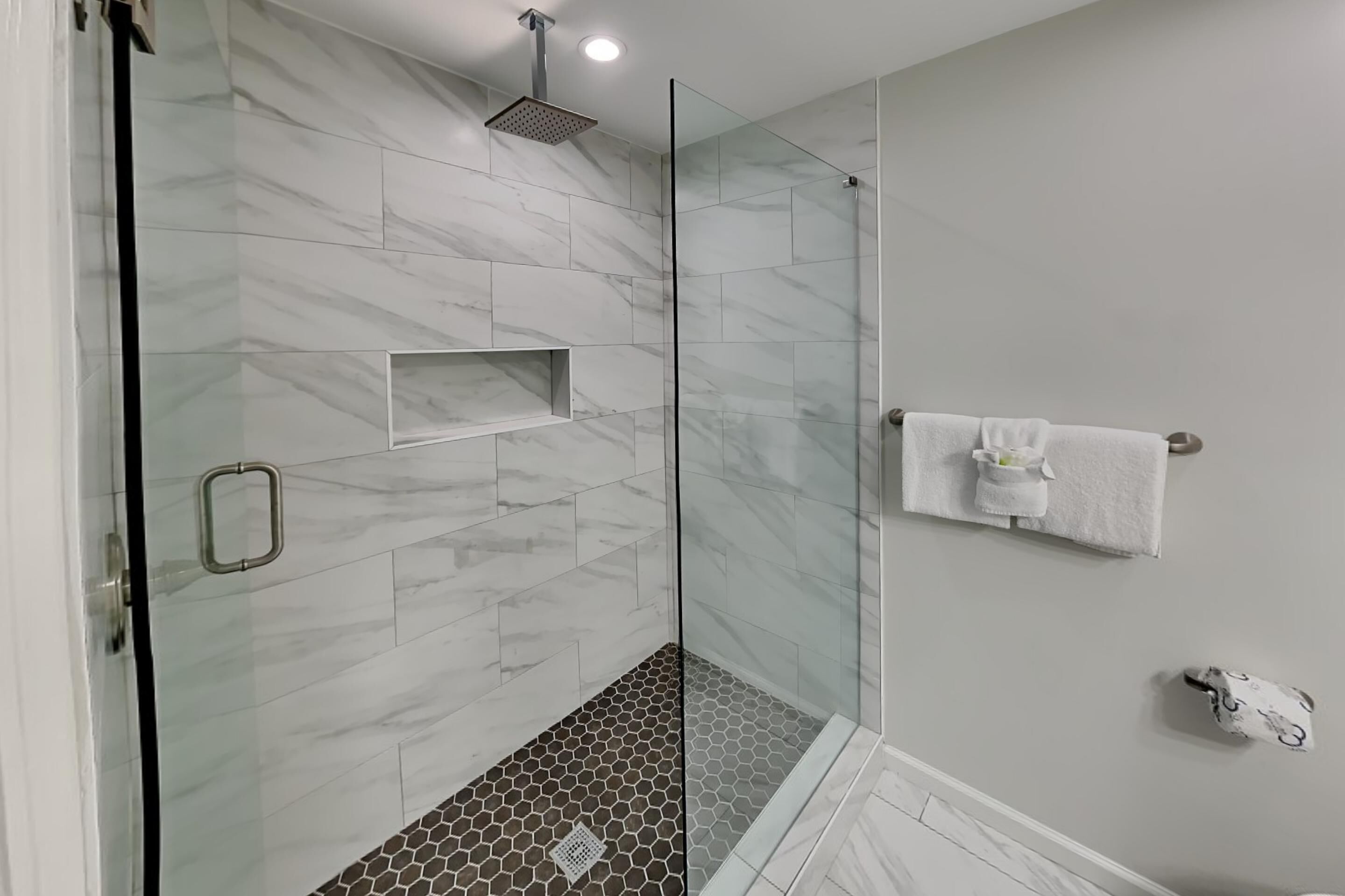 Un baño moderno con cabina de ducha de vidrio, azulejos de mármol y un perchero para toallas.