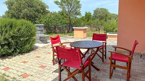 Un patio con una mesa redonda y cuatro sillas rojas, rodeado de follaje y un muro de piedra.