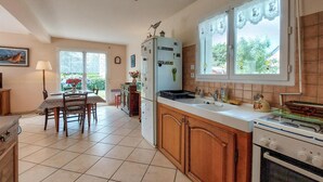 A kitchen with wooden cabinets, a stove, a refrigerator, and a dining area with a table and chairs. - Beach front home in Clohars-Carnoët with WiFi (Clohars-Carnoët)