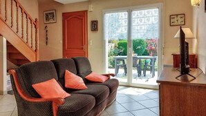 A living room with a sofa, a wooden staircase, a sliding glass door leading to an outdoor area with a table and chairs, and a television on a stand. - Beach front home in Clohars-Carnoët with WiFi (Clohars-Carnoët)