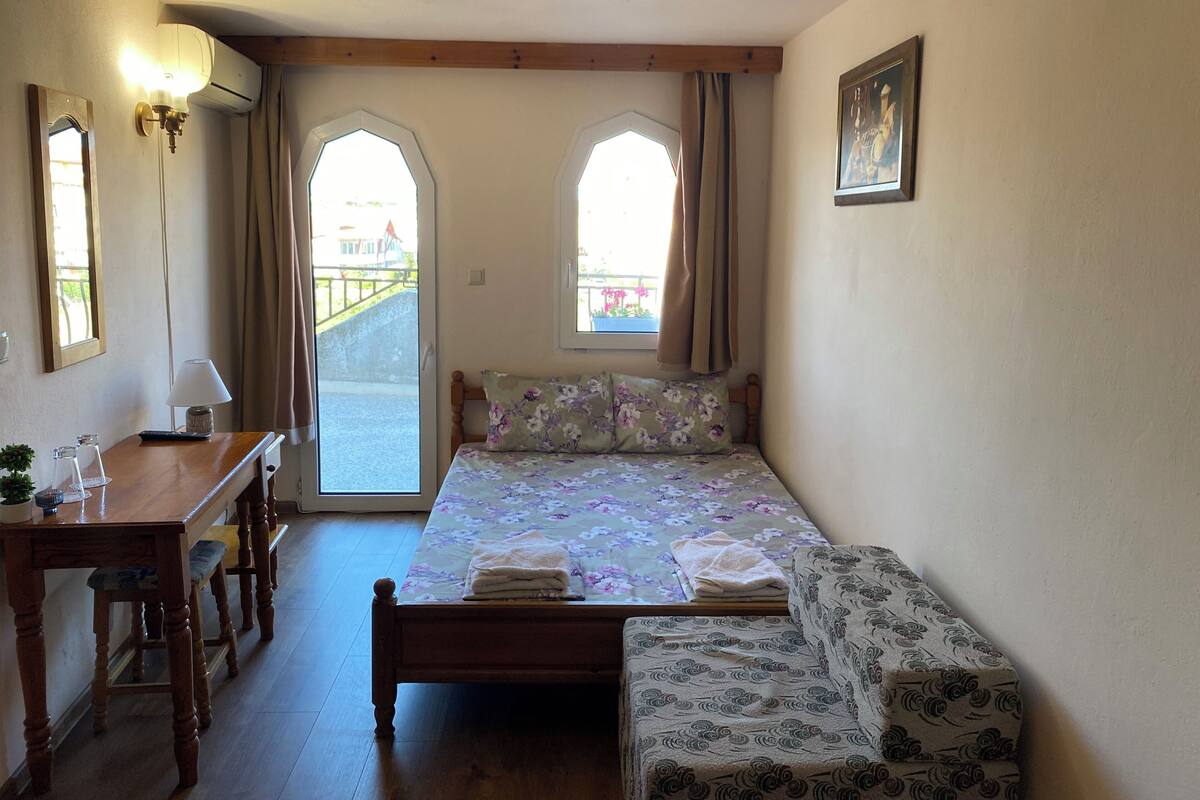 A bedroom with a wooden bed, a wooden desk, a chair, a lamp, and two windows with curtains.