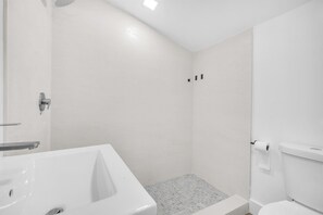 Bathroom features a white bathtub, shower area with glass door, and toilet with a white tank, set against a subtle patterned wall.