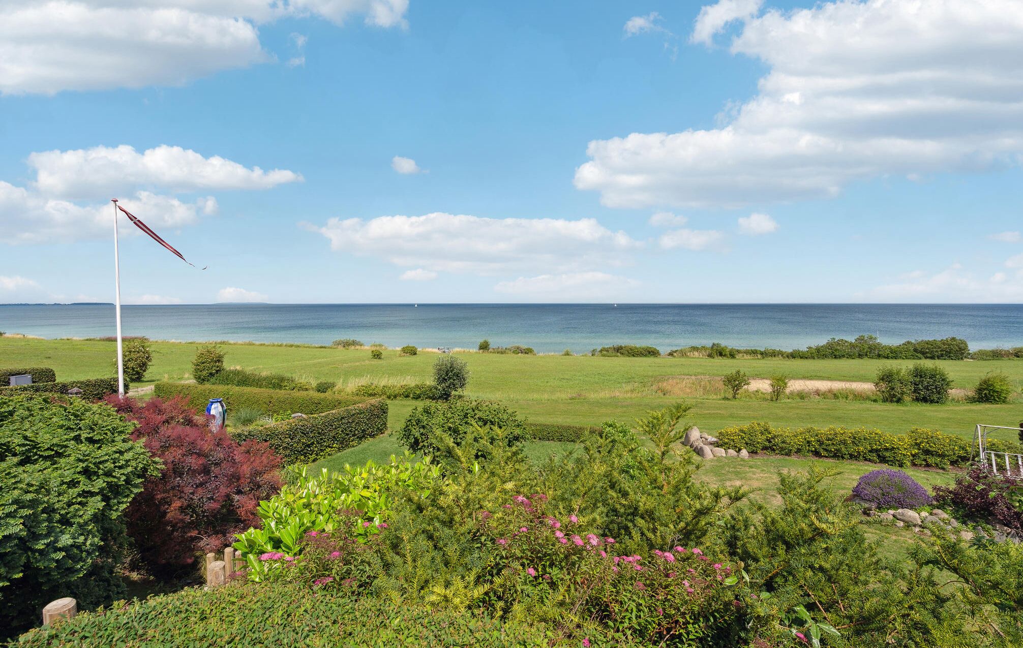 Un paysage côtier avec un champ d’herbe, un mât de drapeau et une vue sur la mer.
