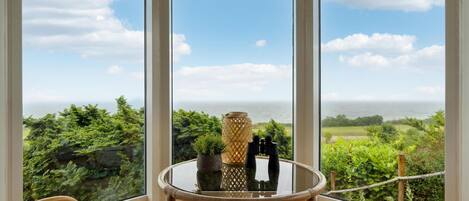 A balcony with a glass table, two chairs, and a view of the ocean.