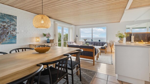 A modern kitchen with a wooden table and chairs, a hanging light fixture, and a view of the sea through large windows. - 2 bedroom cozy home in Nyborg (Nyborg)