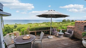 A deck with outdoor furniture, a table, and an umbrella, overlooking a scenic view of the sea and greenery. - 2 bedroom cozy home in Nyborg (Nyborg)