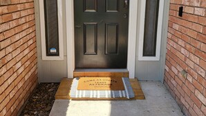 Uma porta de madeira escura com o número '129' acima, um tapete de entrada com uma mensagem acolhedora e uma caixa de correio pequena no lado direito da porta.