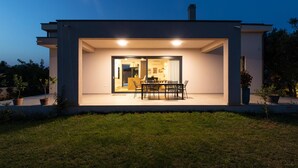 Una casa moderna con zona pranzo, cucina visibile tramite vetrate e patio ben illuminato.