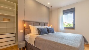Una camera da letto con un letto, un armadio, uno sgabello e vista sul verde.