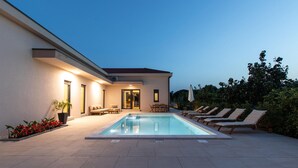 Una casa moderna con piscina, area salotto esterna e patio ben illuminato.