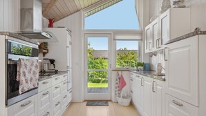 Een keuken met witte kastjes, een roestvrijstalen afzuigkap en uitzicht door een glazen deur naar buiten.