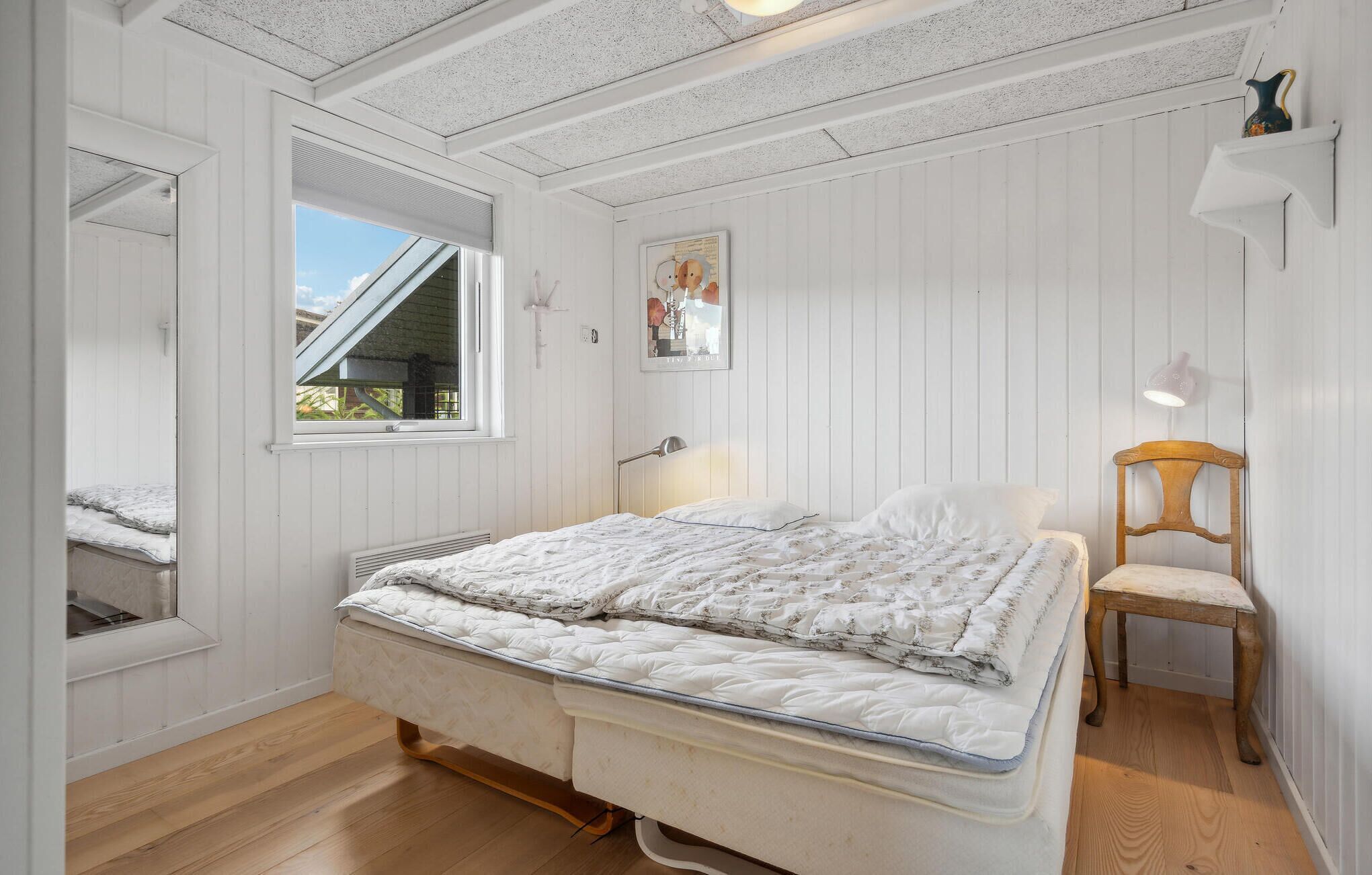 Een slaapkamer met een bed, een stoel, een raam en een foto aan de muur.