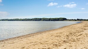 Een zandstrand met kalm water en een bebost eiland in de verte.