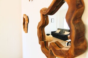 Ein Spiegel zeigt einen Raum mit einer schwarzen Couch, einem runden Rattan-Pouff und einem kleinen Tisch.