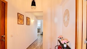 Um corredor com piso de madeira, uma mesa preta com flores cor-de-rosa e um relógio de parede.