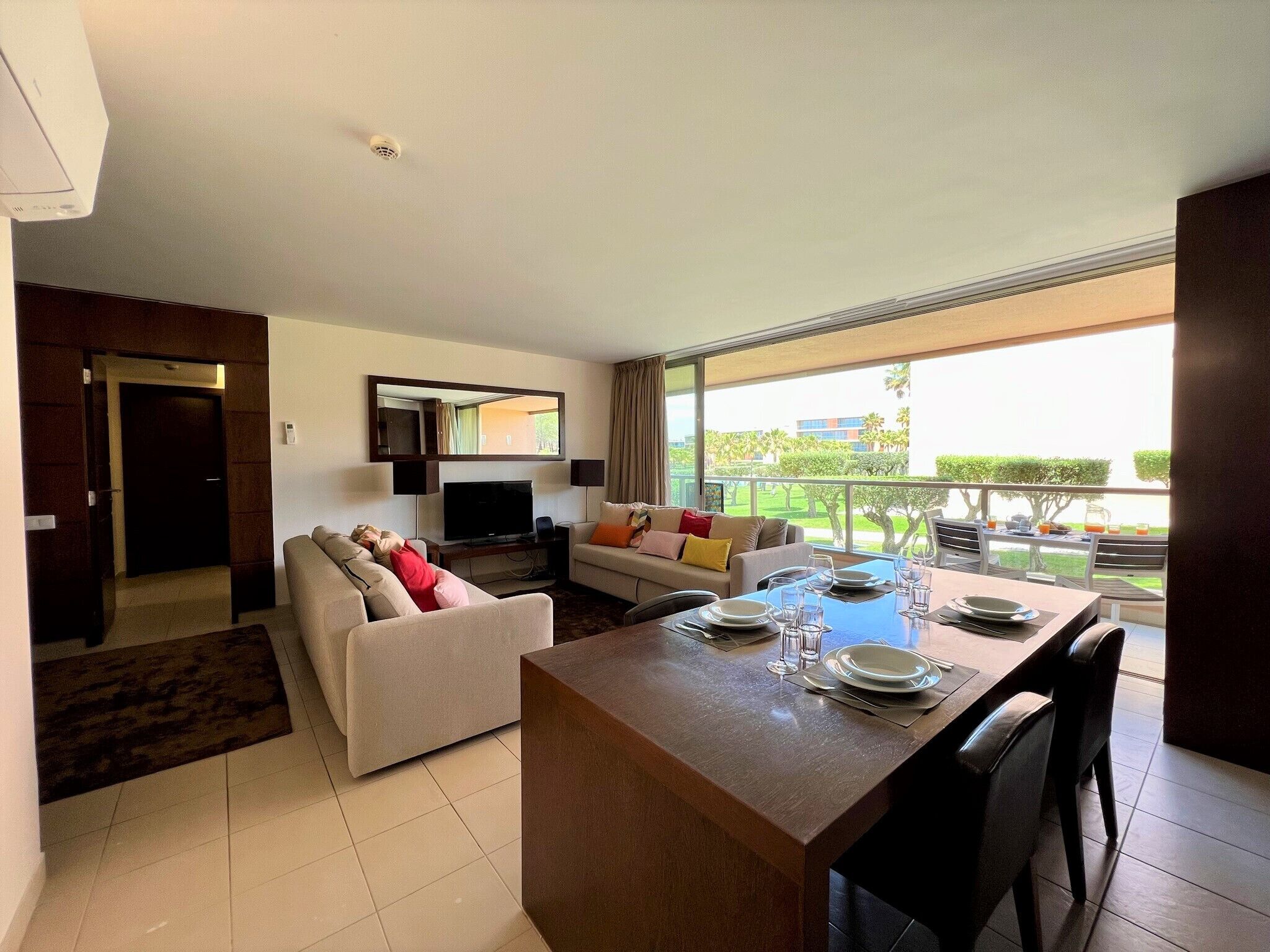 Una sala de estar moderna con comedor, televisor y balcón con vistas al exterior.
