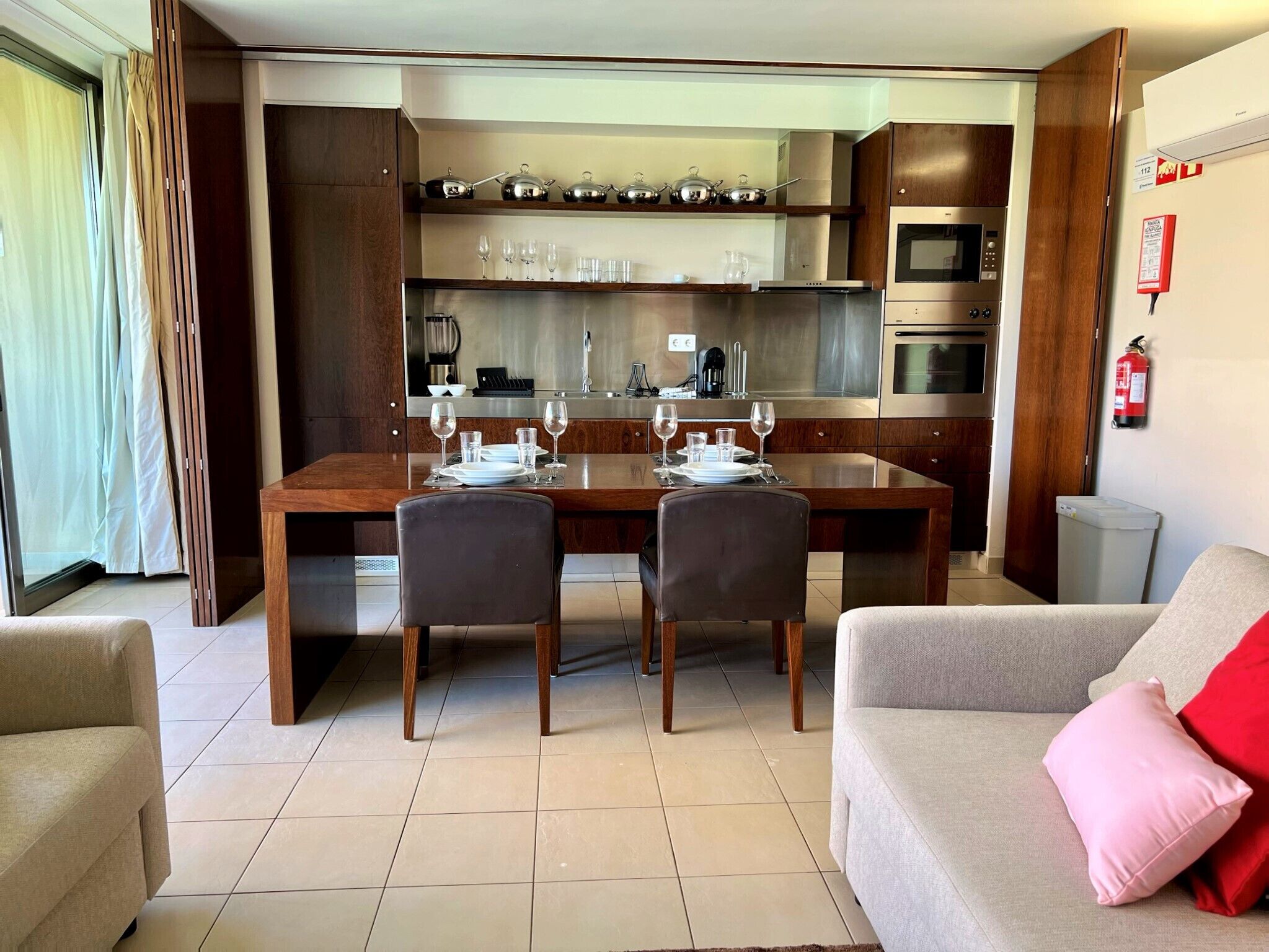 A modern kitchen with a dining table set for four, a sofa, and a fire extinguisher on the wall.