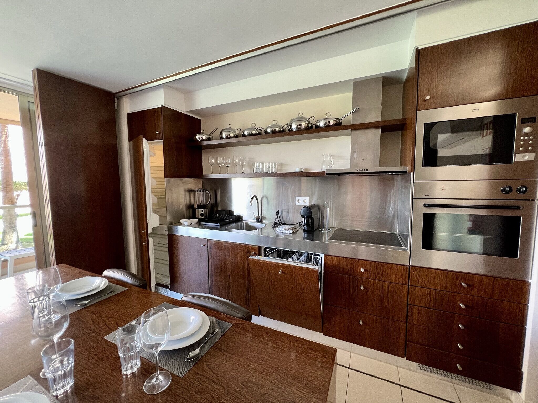 A modern kitchen with stainless steel appliances, wooden cabinets, and a dining area set for four.