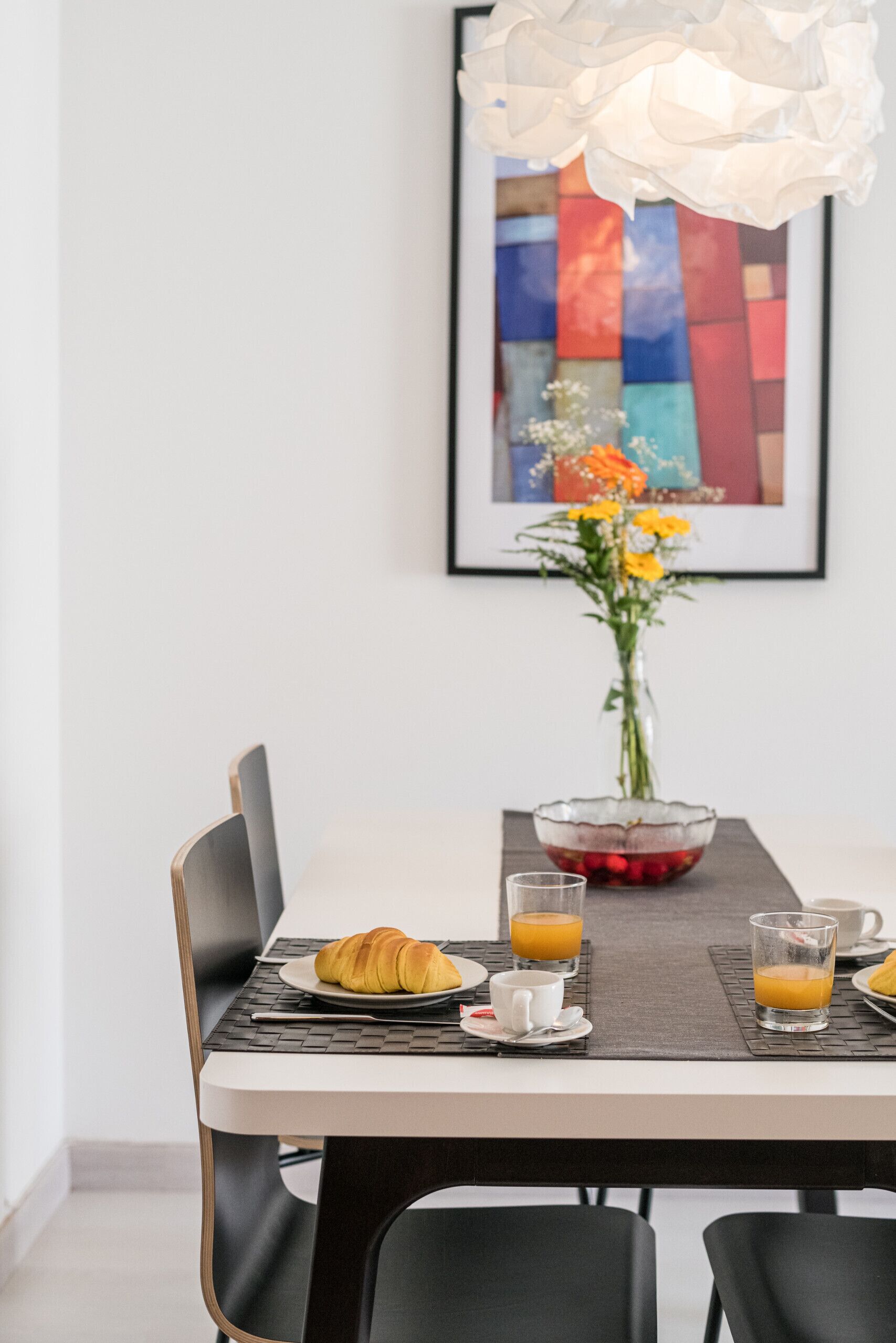 A dining table with a laptop, croissant, and glasses of orange juice.