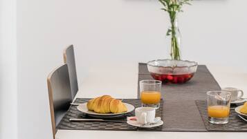 A dining table with a laptop, croissant, and glasses of orange juice.