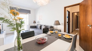 A modern hotel room with a dining area, a sofa, a laptop, and a breakfast setup. - Lagos Classic by Homing (Lagos)