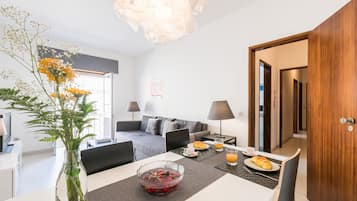 A modern hotel room with a dining area, a sofa, a laptop, and a breakfast setup.