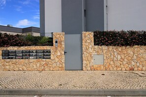 Ein Gebäudeeingang mit einer Steinmauer, einem Metallgitter und einem gepflasterten Weg.