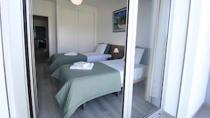Een hotelkamer met twee bedden, een schilderij aan de muur en een deur naar een andere kamer.