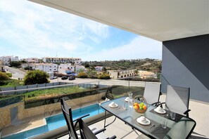 Ein Balkon mit einem Glastisch, gedeckt für ein Essen, mit Blick auf einen Swimmingpool und eine Wohngegend.