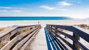 A wooden boardwalk leading to a beach with a clear blue sky and ocean.