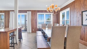 A dining area with a wooden table and chairs, a chandelier, and large windows with a view.