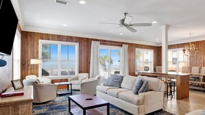 A spacious living room with a wooden paneled wall, a ceiling fan, and a large window overlooking a balcony.