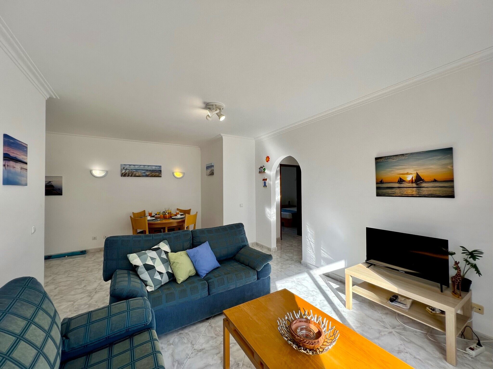 A living room with a sofa, a coffee table, a TV, and a dining area with a table and chairs.