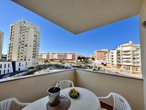Un balcon avec une table, une bouteille de champagne et un saladier de fruits.