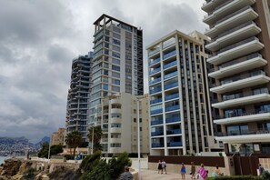 Un moderno edificio de gran altura con varios balcones, vistas al mar y un sendero de piedra que conduce a la entrada.