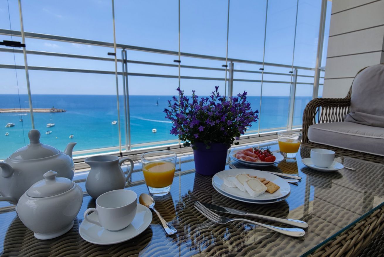 Una mesa de desayuno con juego de té, una planta en maceta y vista al mar.