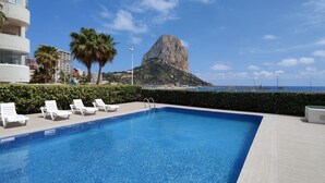 A swimming pool with lounge chairs, a palm tree, and a rocky hill in the background. - BAUPRES luxury apartment (Calpe)