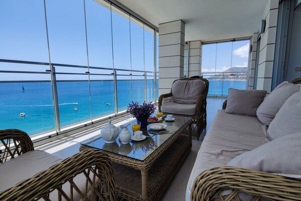 Un balcón con mobiliario de mimbre, una mesa con alimentos para el desayuno y vista al mar.
