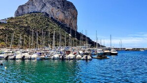 A marina with boats docked, a rocky hill in the background, and a clear blue sky. - BAUPRES luxury apartment (Calpe)