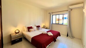 Una camera d'hotel con un letto, due comodini, una finestra con tende e un condizionatore d'aria a muro.