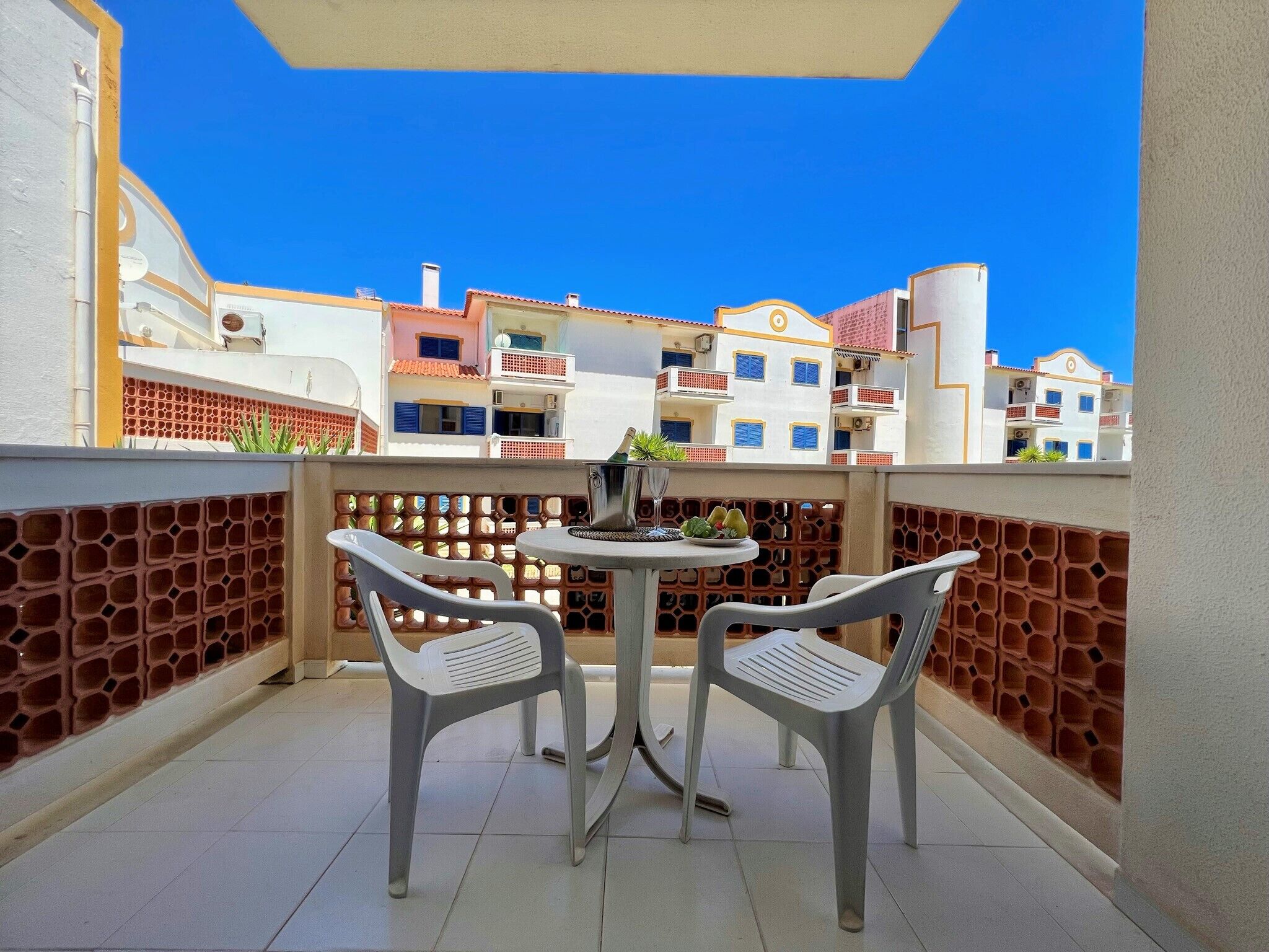 A balcony with two chairs and a table, overlooking a row of colorful buildings.