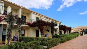 Fila de edificios de hotel con balcones, un paseo de baldosas y setos bien cuidados.