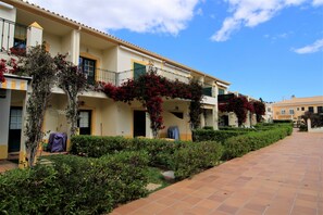 Fila de edificios de hotel con balcones, un paseo de baldosas y setos bien cuidados.