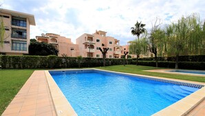 Una piscina con bordes de azulejos, rodeada por un césped cuidado y setos.