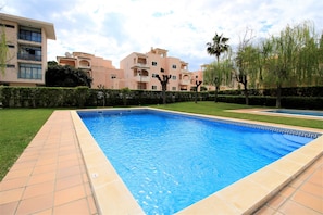 Una piscina con bordes de azulejos, rodeada por un césped cuidado y setos.