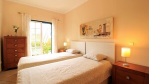 Habitación de hotel con dos camas, un aparador, un cuadro en la pared y una ventana con cortinas.